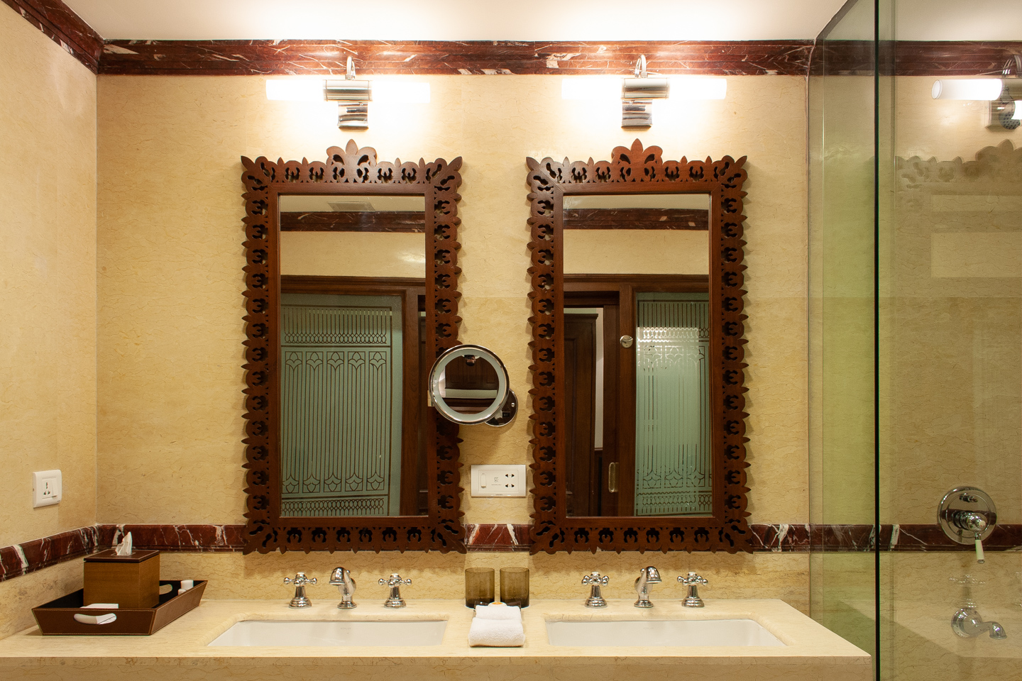 The marble walls of the bathroom are highlighted with trim of carved red marble. The tub has a sliding glass screen.
